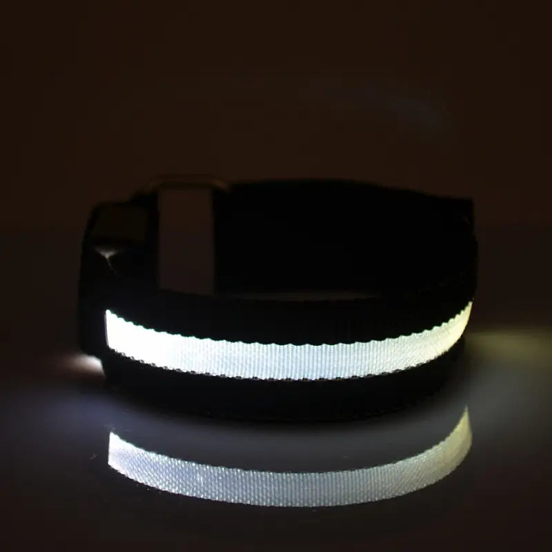 Collar negro reflectante para perro con una franja blanca ancha y brillante, presentado como parte de un producto de brazalete de seguridad LED recargable por USB para correr.