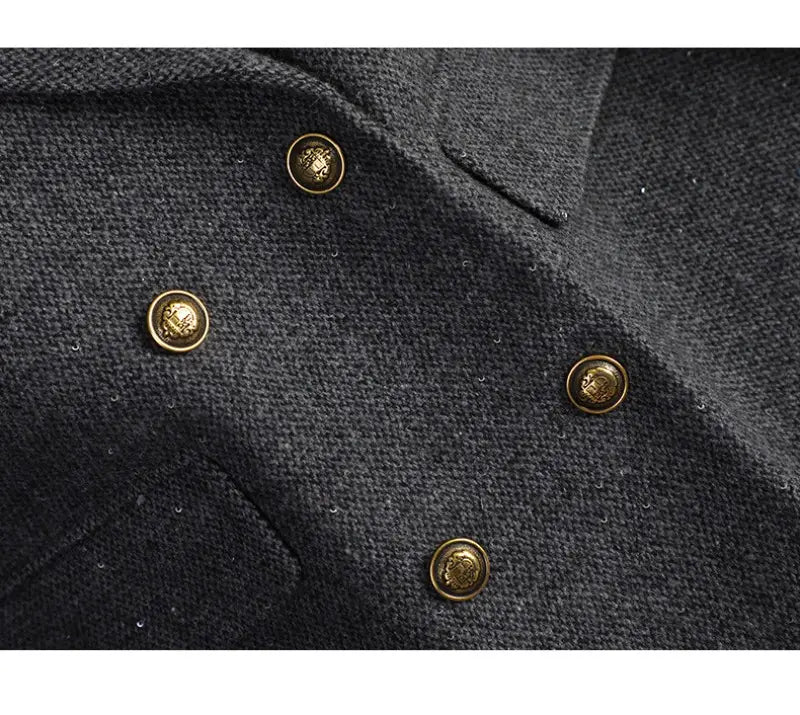 Gold-toned buttons with embossed crest designs adorn the dark gray wool blend fabric of a double breasted blazer.