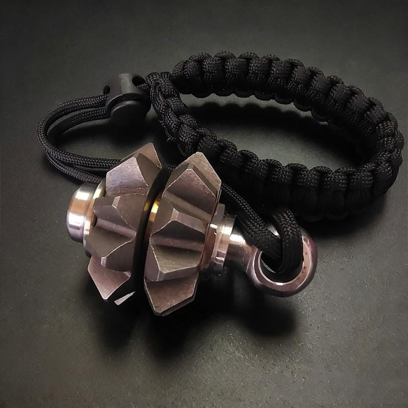 Black paracord bracelet with a metallic gear-shaped pendant featuring angular facets and a brushed silver finish for use as a gear fidget spinner keychain and emergency survival tool.