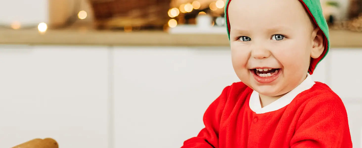 Ein fröhliches Baby, das eine rote und grüne Elfenmütze mit passender roter Kleidung trägt, in Verbindung mit einem Weihnachtsüberraschungs-Adventskalender-Bausteinset.