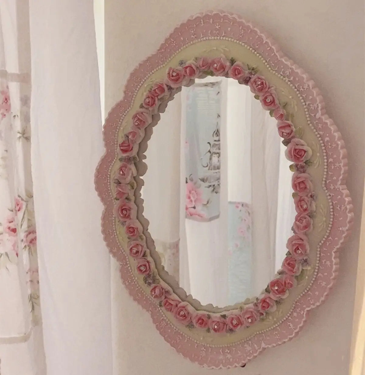 Espejo de pared ovalado barroco color rosa con un delicado marco con borde de encaje rosa, adornado con rosas rosas en relieve y adornos tipo perla para decoración floral vintage.
