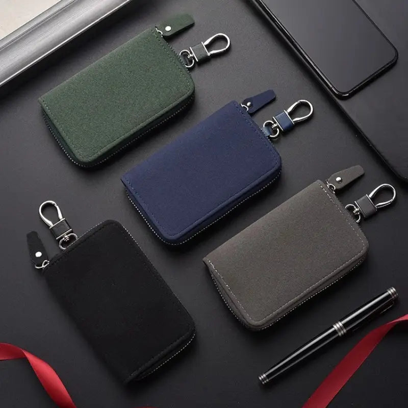 Four compact leather key holder organizer pouches in dark green navy blue black and gray suede-like fabric with silver-toned metal clasps.