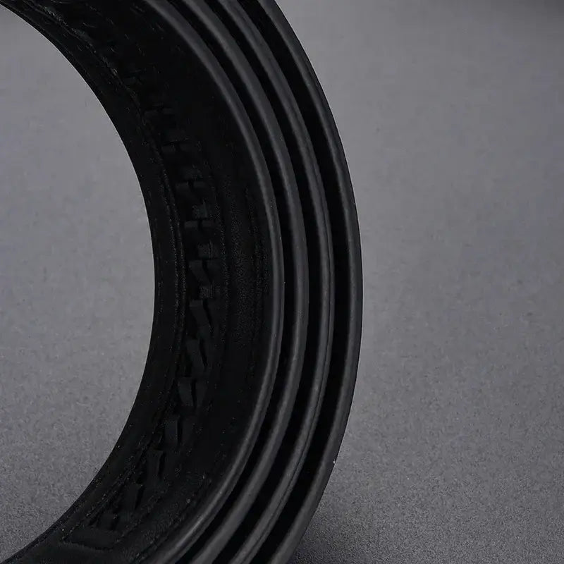 black rubber tire with textured tread pattern and concentric ridges along the sidewall shown alongside a mens automatic leather belt with silver buckle.