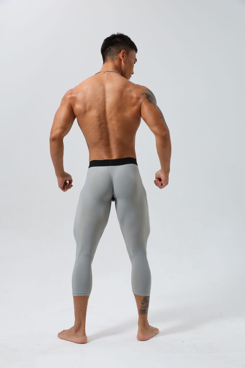 背面側から見せた、黒いウエストバンド付きのグレーメンズ用ナイロンフィットネスタイツ、トレーニングパンツ。体にフィットするデザインです。