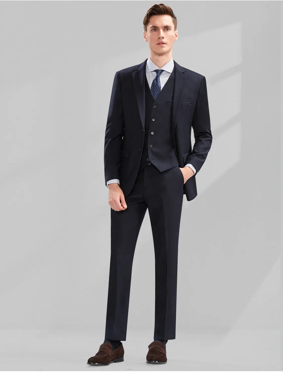 Un homme portant un costume bleu marine foncé pour homme en coupe slim, formel et professionnel décontracté, avec un type de fermeture assorti comprenant un gilet et un pantalon, associés à une chemise habillée bleu clair et à une cravate à motifs.