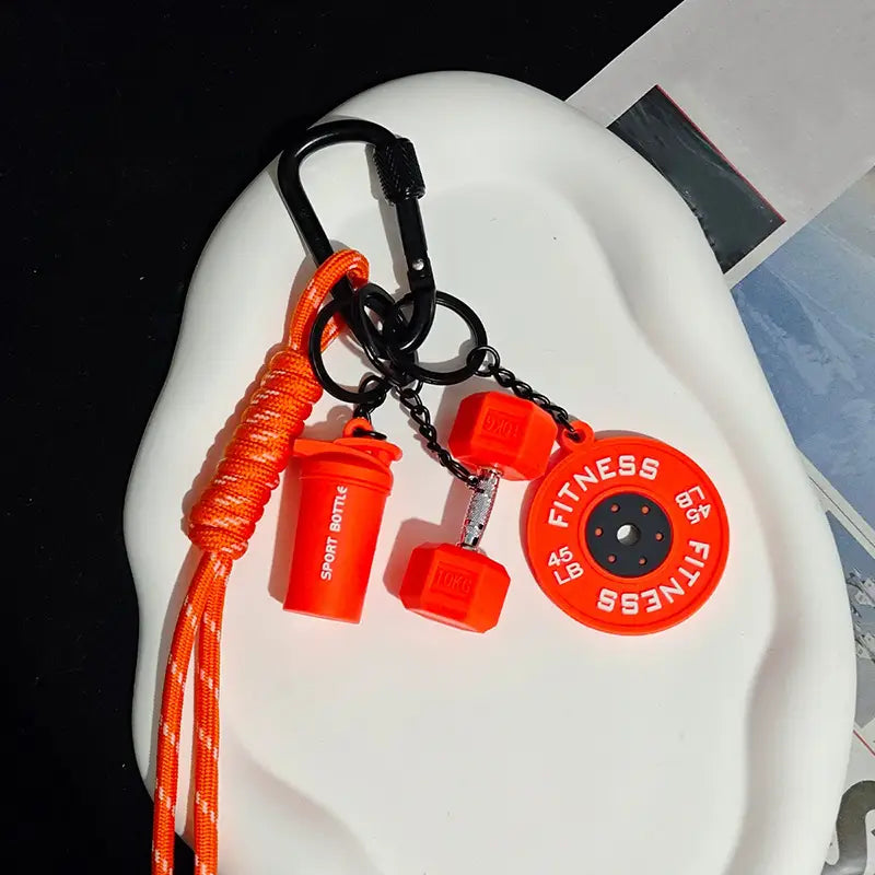 Un porte-clés de fitness vibrant orange en silicone, comprenant des breloques d’haltère, de disque de poids et de bouteille shaker, conçu comme accessoire de sac de sport.