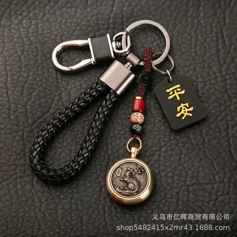 中国の干支をモチーフにした編みレザー製ラッキーペンダントのコレクションより。黒いタグに金色の漢字が刻まれたブロンズのコインチャーム、赤と黒のビーズを備えた黒の編みレザー製キーチェーン。