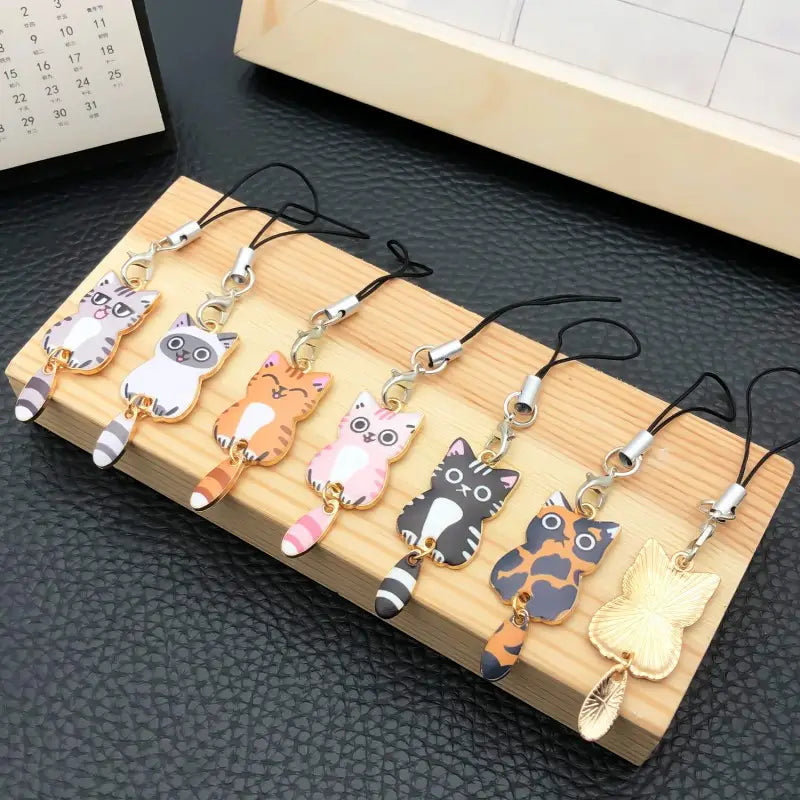a set of colorful enamel cat keychains featuring cartoon-style charms with black cords and metallic clasps for phone decoration