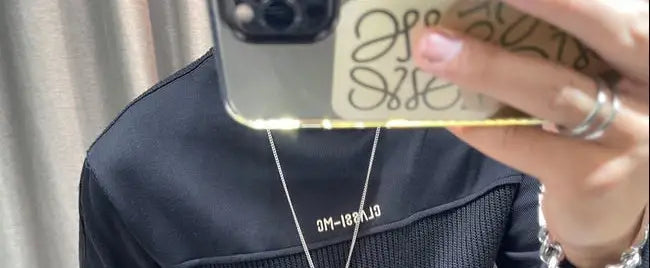 Étui de téléphone transparent avec un logo en relief embossé, rehaussé d’or, présenté aux côtés d’un pull-over en maille à empiècement contrastant pour homme, manches longues.