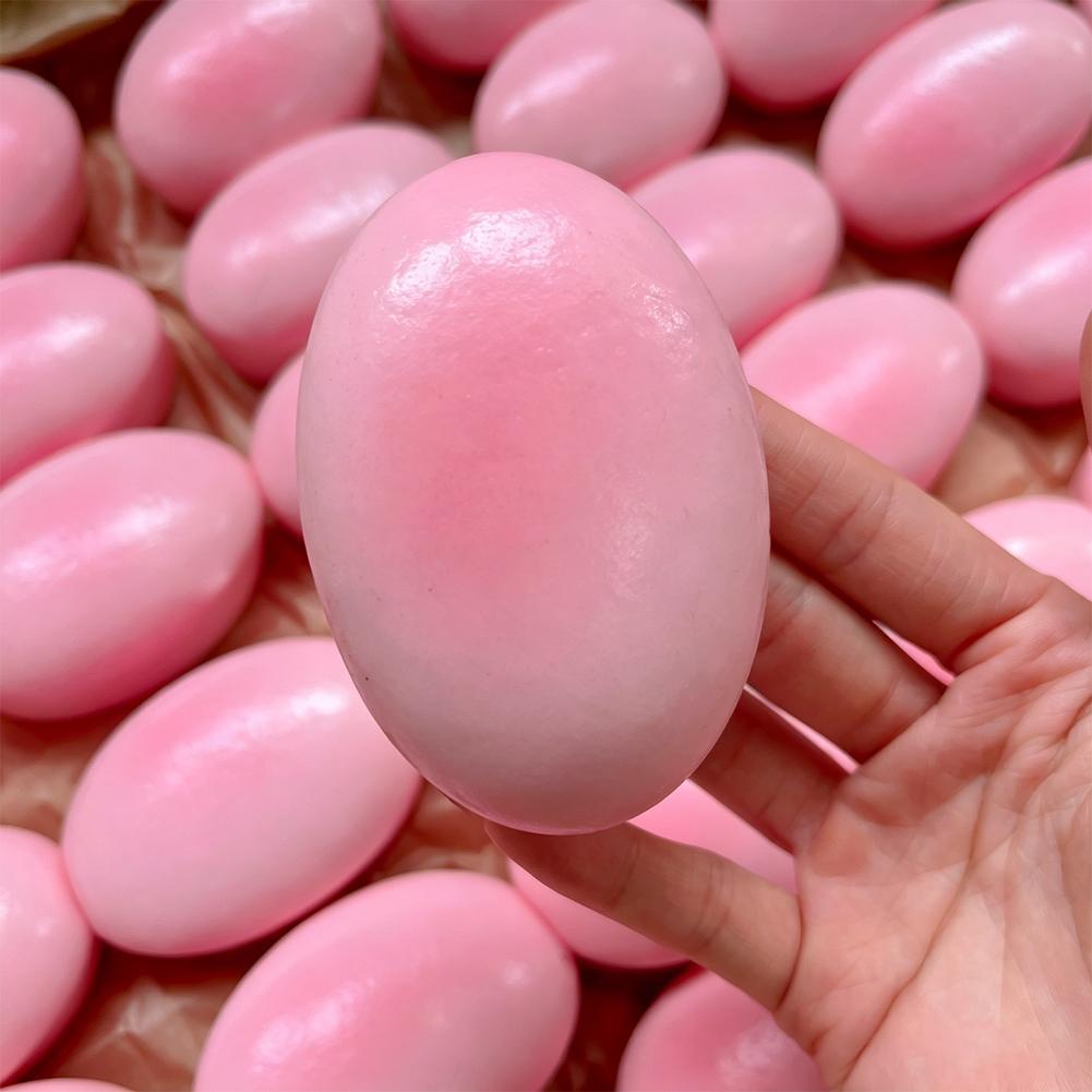Una mano sostiene un juguete esponjoso y blando de color rosa brillante para aliviar el estrés y lento en elevarse, con contornos suavemente redondeados y una superficie ligeramente reflectante.
