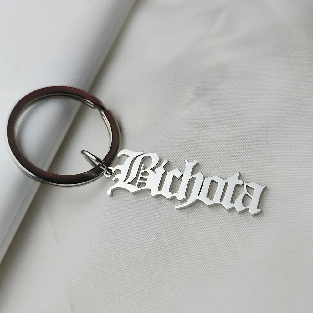 Llavero de nombre personalizado de metal plateado, hecho de joyería de acero inoxidable, con el nombre «richota» grabado en una tipografía gótica ornamental.