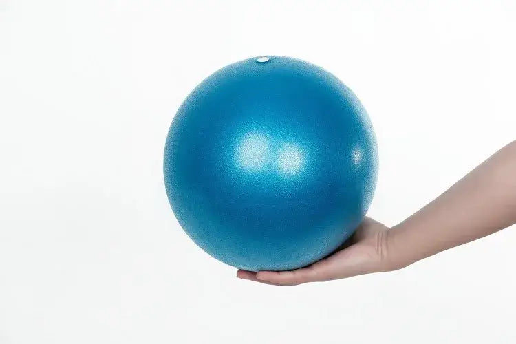 A smooth matte-finish blue anti-burst yoga ball held gently in a hand designed for balance training with superior air leakage protection.