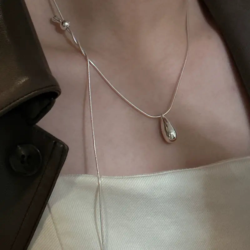 Collier goutte de larmes en argent sterling présentant un pendentif argenté épuré, un design minimaliste et une chaîne fine au fini lisse et réfléchissant.