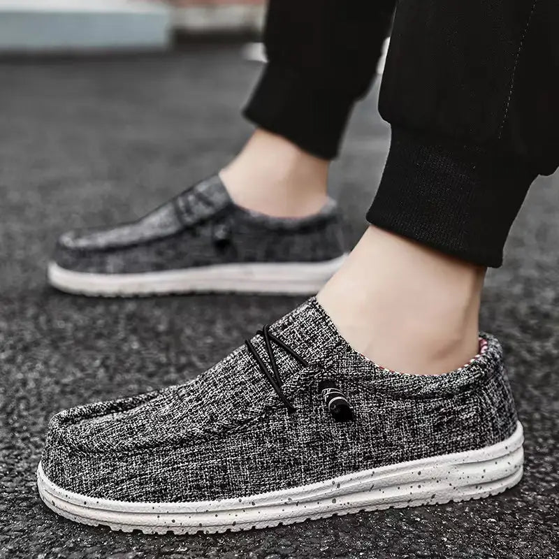 Chaussures décontractées de type mocassins à enfiler en toile pour hommes, en toile texturée grise et noire, avec des semelles blanches à motifs d’aspérités.
