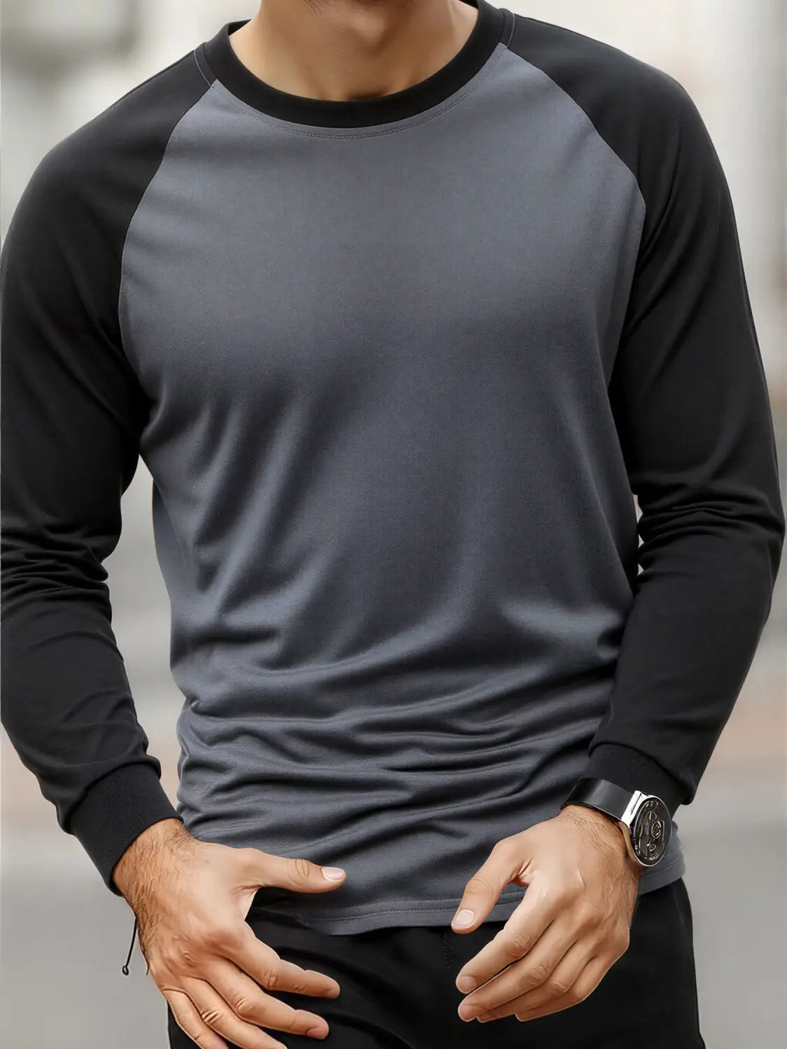 Ein Herren-Raglanshirt mit langem Ärmel in Dunkelgrau und Schwarz mit geripptem Rundhalsausschnitt und glattem Material, das sich ordentlich über den Oberkörper legt.