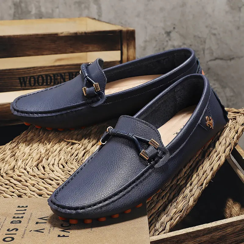 Chaussures à enfiler habillées en cuir bleu marine pour hommes, avec des boucles métalliques ton or et des semelles en caoutchouc orange, conçues pour un port décontracté sans effort.