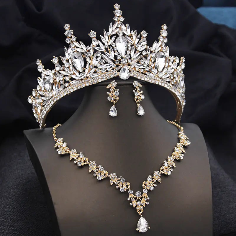Une couronne de mariée étincelante en or et cristaux transparents, avec des motifs de feuillage et des boucles d’oreilles et un collier assortis pour des accessoires de mariage.