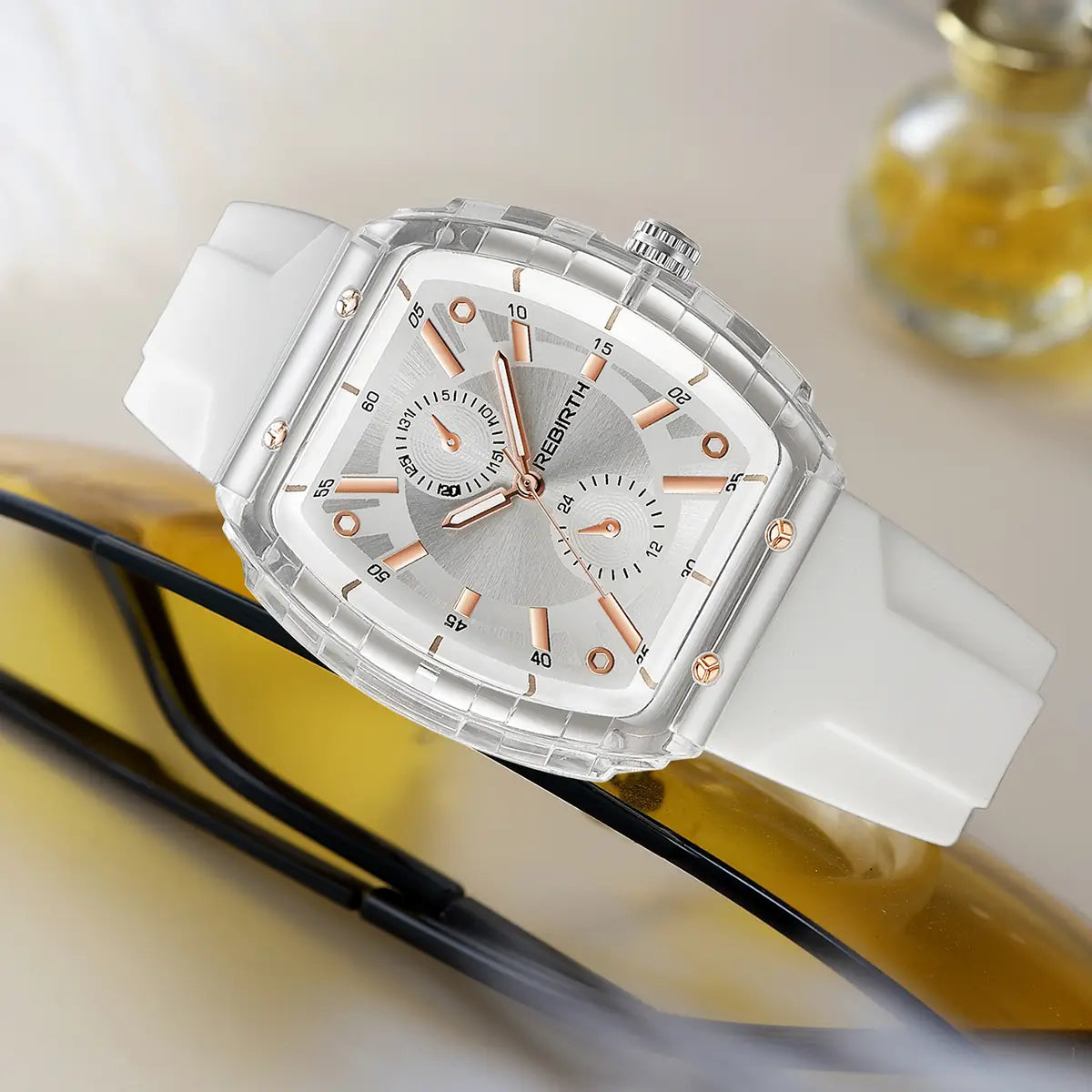 A silicone casual watch with a rose gold rectangular dial featuring a sleek white resin body, a transparent case, and multiple subdials on its silver-toned face.