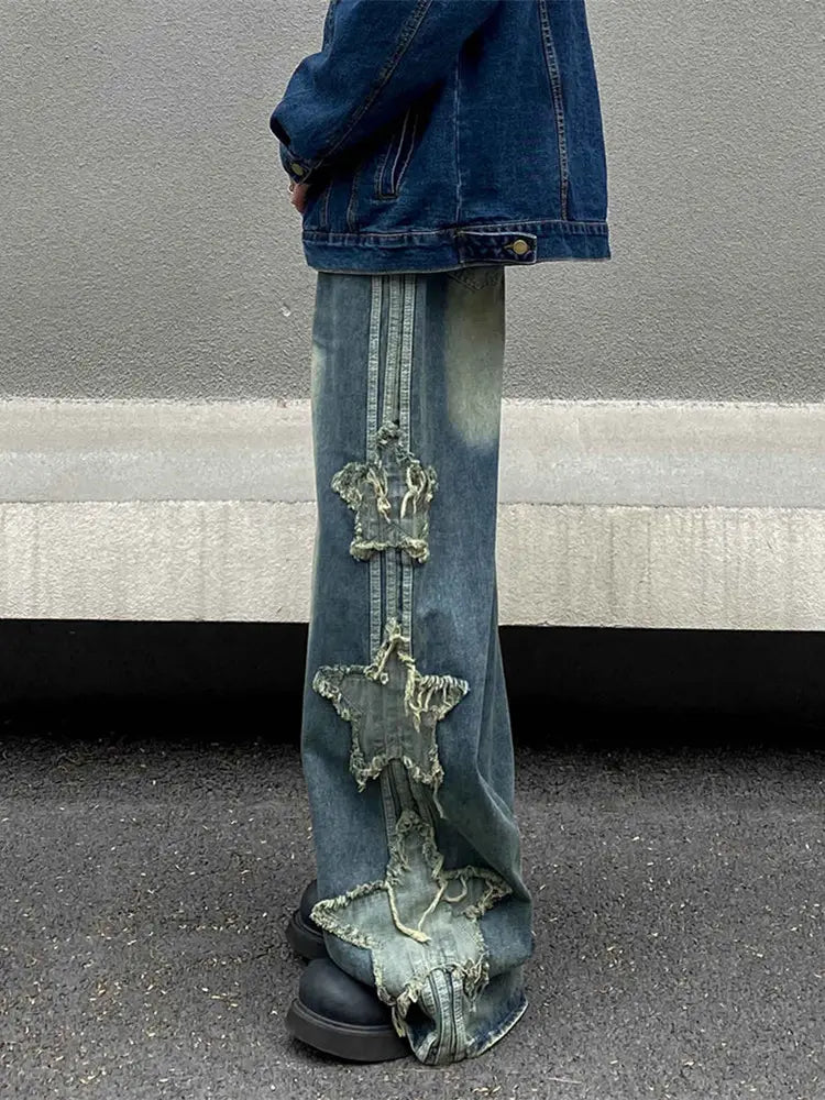 Jeans en denim délavé et déchiré baggy style y2k bleus, avec une rangée verticale de trois patchs en forme d’étoiles effilochés le long de la jambe extérieure.