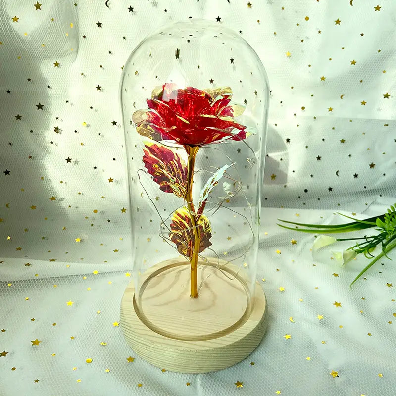 Eine kräftig rote Rose mit Goldfolien-Details, umschlossen in einer klaren Glaskuppel auf einem hellen Holzsockel, im „Eternal Gold Rose Glass Dome LED Light Gift“.