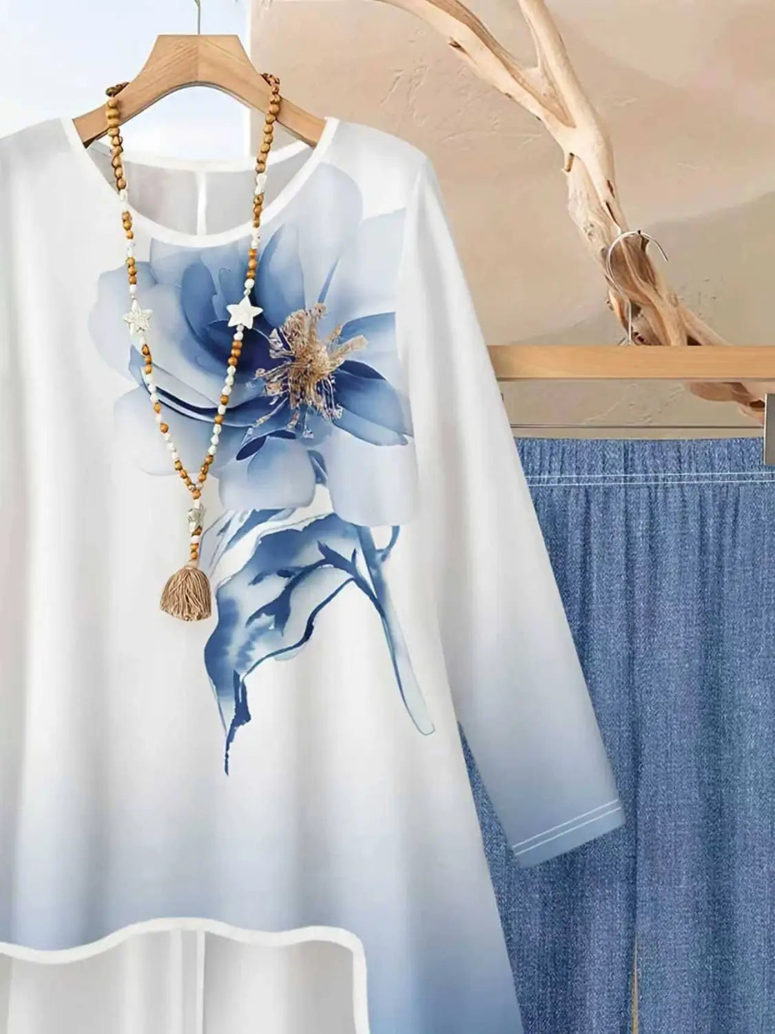 Weißes Langarmoberteil mit transparentem Overlay und großem blauem Blumendruck als Teil eines zweiteiligen Outfits mit Blumendruck und weitem Bein.