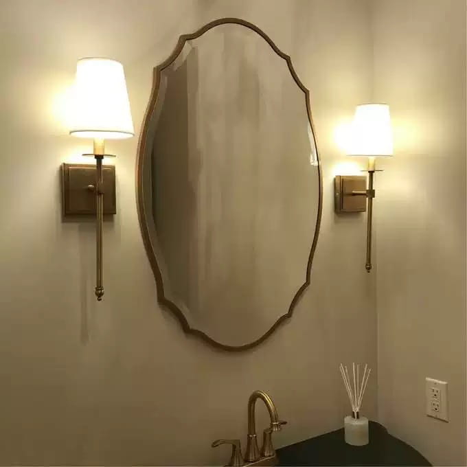 Miroir de salle de bains ovale à cadre doré, bords à volutes, mettant en valeur un style de miroir ornemental pour une décoration murale.