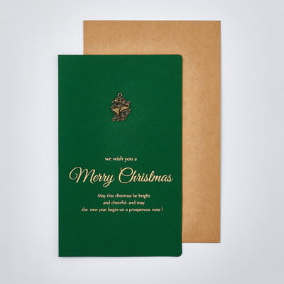 Deep green Christmas greeting card with gold foil lettering and a small metallic bell emblem paired with gold foil envelopes.