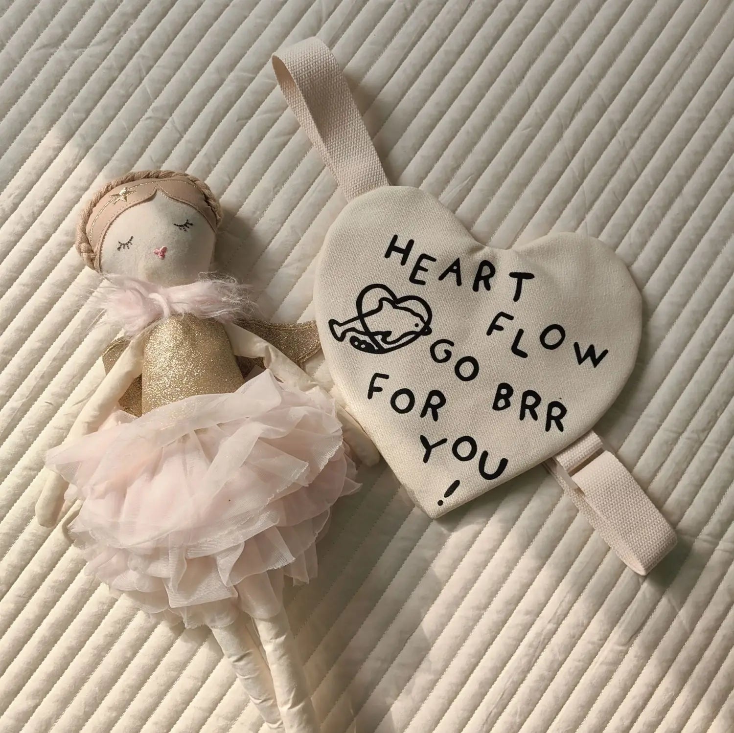 Eine weiche cremefarbene herzförmige Pouch-Umhängetasche für koreanische Kinder mit schwarzem besticktem Text und kleinem Vogel-Design.