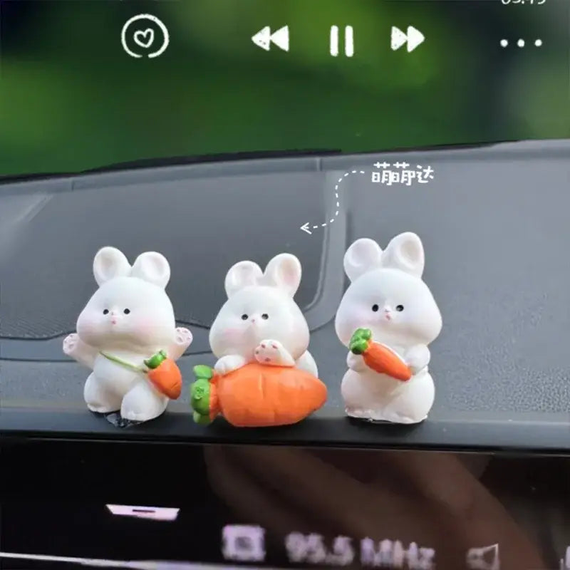 Trois figurines de lapin en résine blanches tenant ou à côté de carottes orange, comme des ornements de tableau de bord de voiture en forme de lapin mignon.