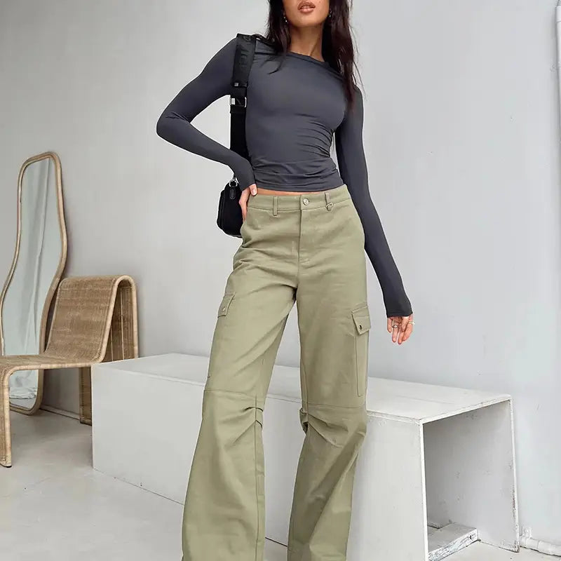Pantalones cargo color verde oliva con múltiples bolsillos y corte de pierna recta, combinados con una blusa corta ajustada tipo slim fit para mujer, con mangas largas fruncidas.
