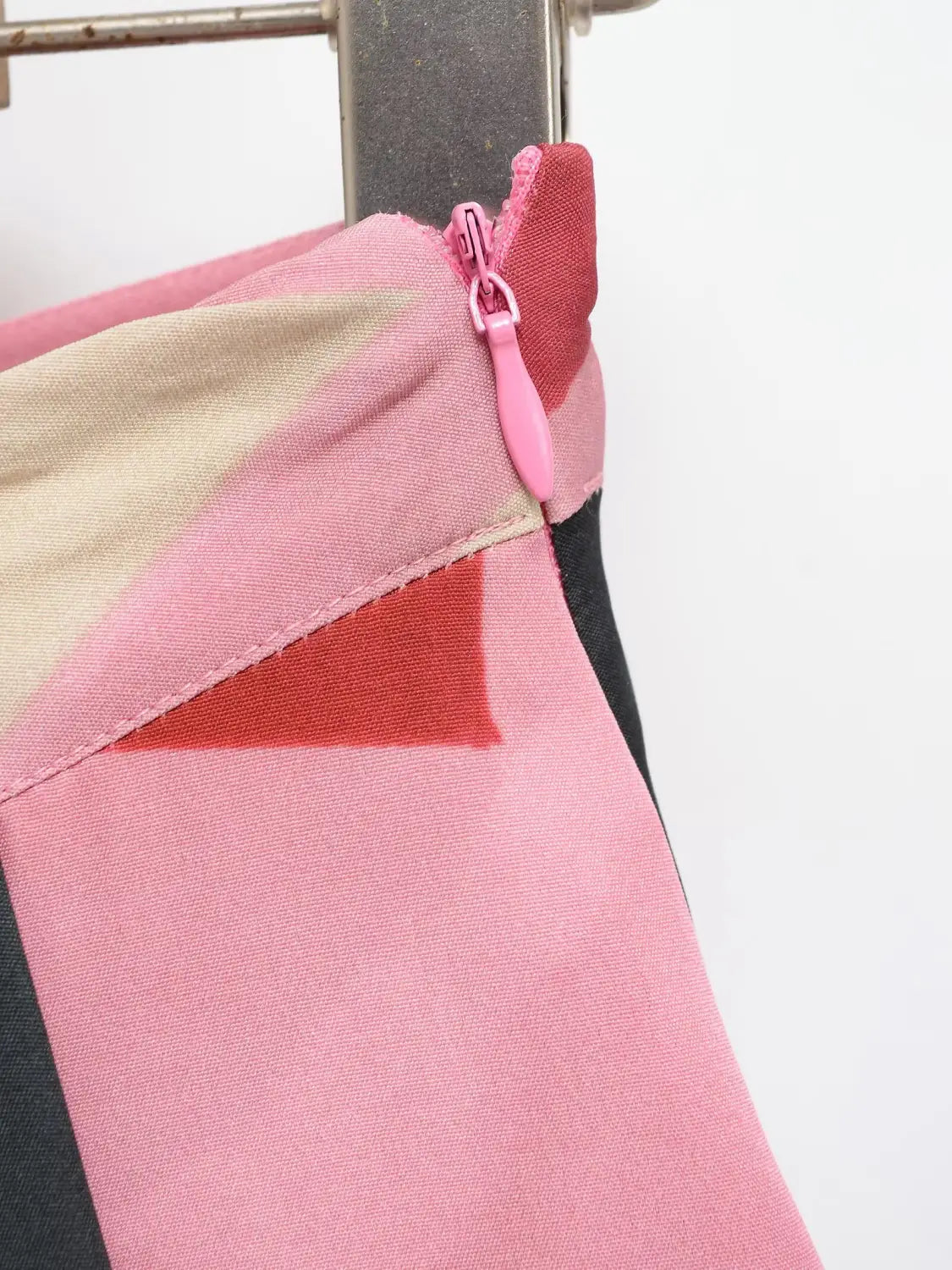 Ein geometrischer Satin-Midirock mit geometrischen Mustern in Rosa, Beige und Schwarz sowie einem passenden rosa Reißverschluss-Anhänger