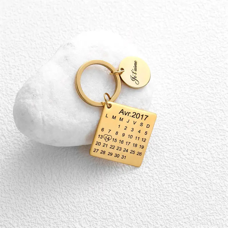 Gold-colored metal personalized calendar keychain featuring a square charm for April 2017 and a small round disc engraved with je taime ideal as a custom anniversary gift.