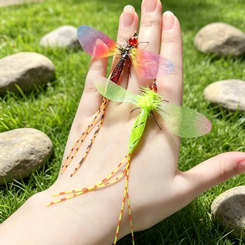 zwei farbenfrohe Libellen-Cat-Toy-Ersatzkopf-Teile mit kunstvoll gefertigten schillernden rosa- und blauen Flügeln und einem roten Körper sowie durchscheinenden grünen Flügeln mit einem leuchtend limettengrünen flauschigen Hinterleib, der sanft auf einer geöffneten Handfläche ruht