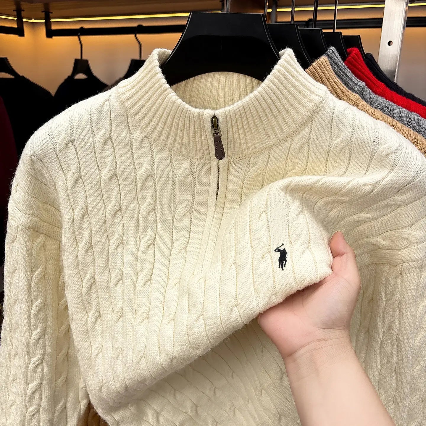 Herren-Designer-Sweater aus cremefarbenem Zopfmusterstrick mit halbem Reißverschluss, mit kleinem schwarzem besticktem Polo-Spieler-Logo auf der Brust.
