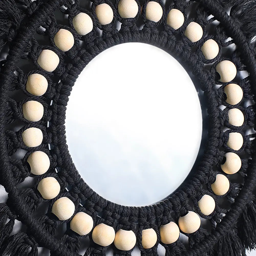 Black round macrame wall mirror with light-colored wooden beads and fringe offering a boho decorative mirror design.