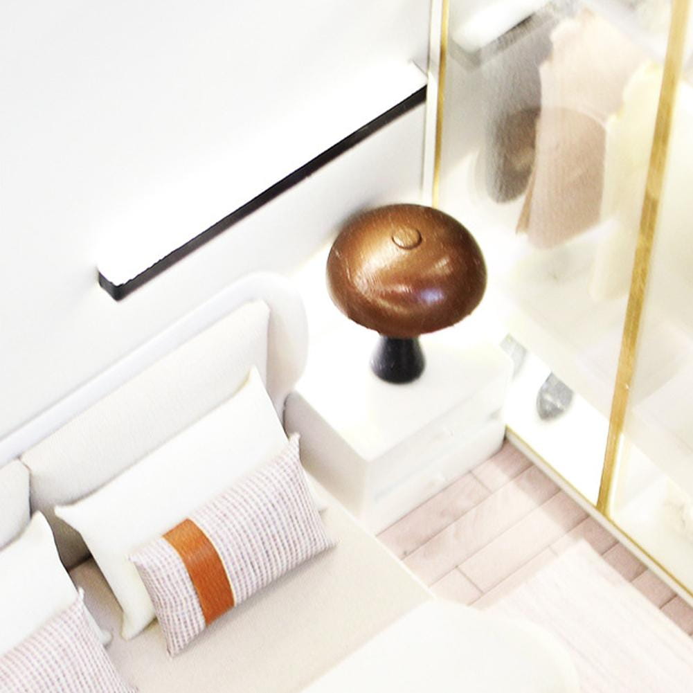 A polished bronze mushroom-shaped table lamp with a black base shown with a miniature dollhouse double bed featuring cream style bedding.