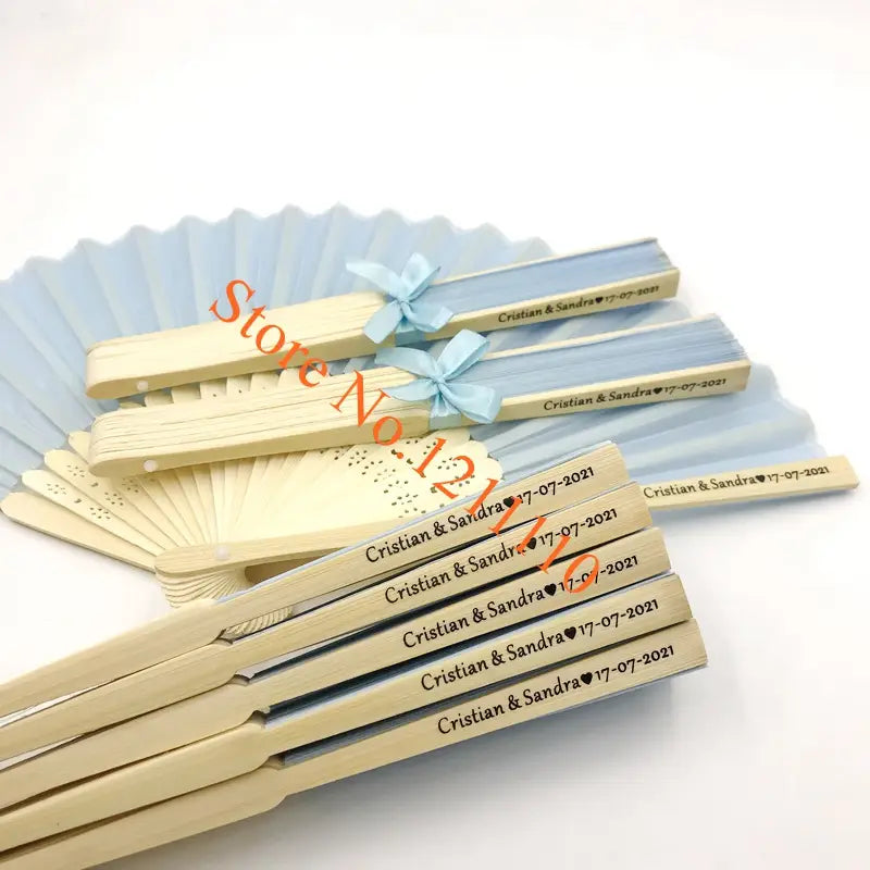 Light blue and cream-colored wooden folding fans with delicate light blue ribbon ties made of bamboo and silk for custom wedding hand fans personalized favors.