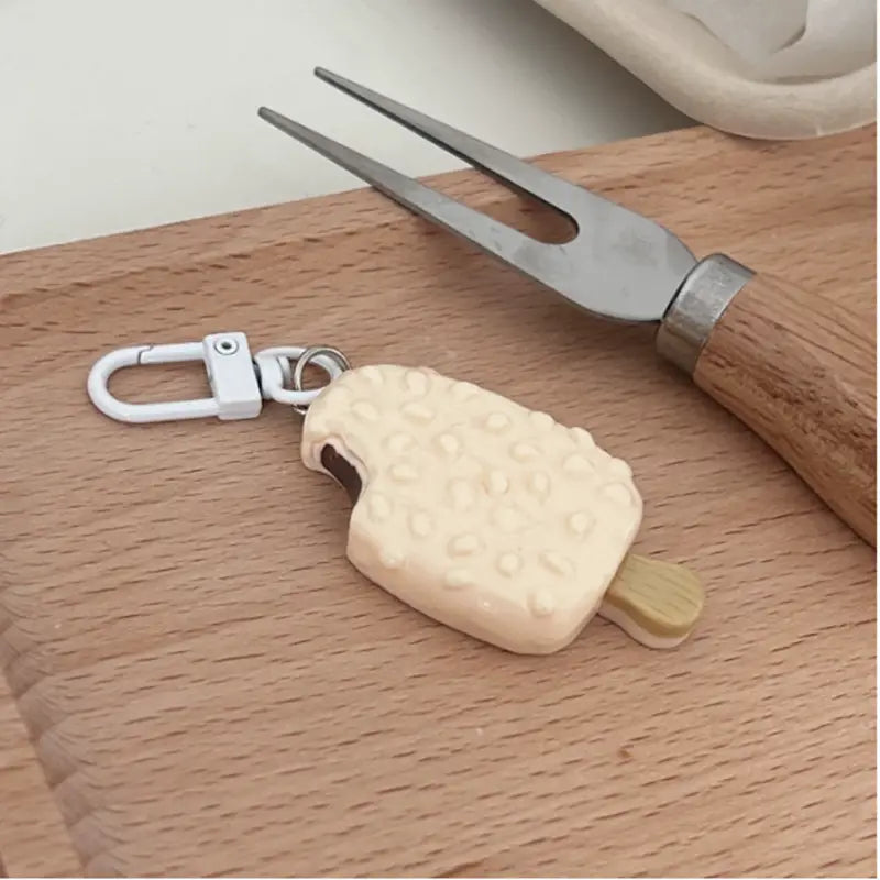 Cream-colored textured ice cream pop keychain with a wooden stick and silver carabiner for bag pendant in chocolate biscuit cartoon design.