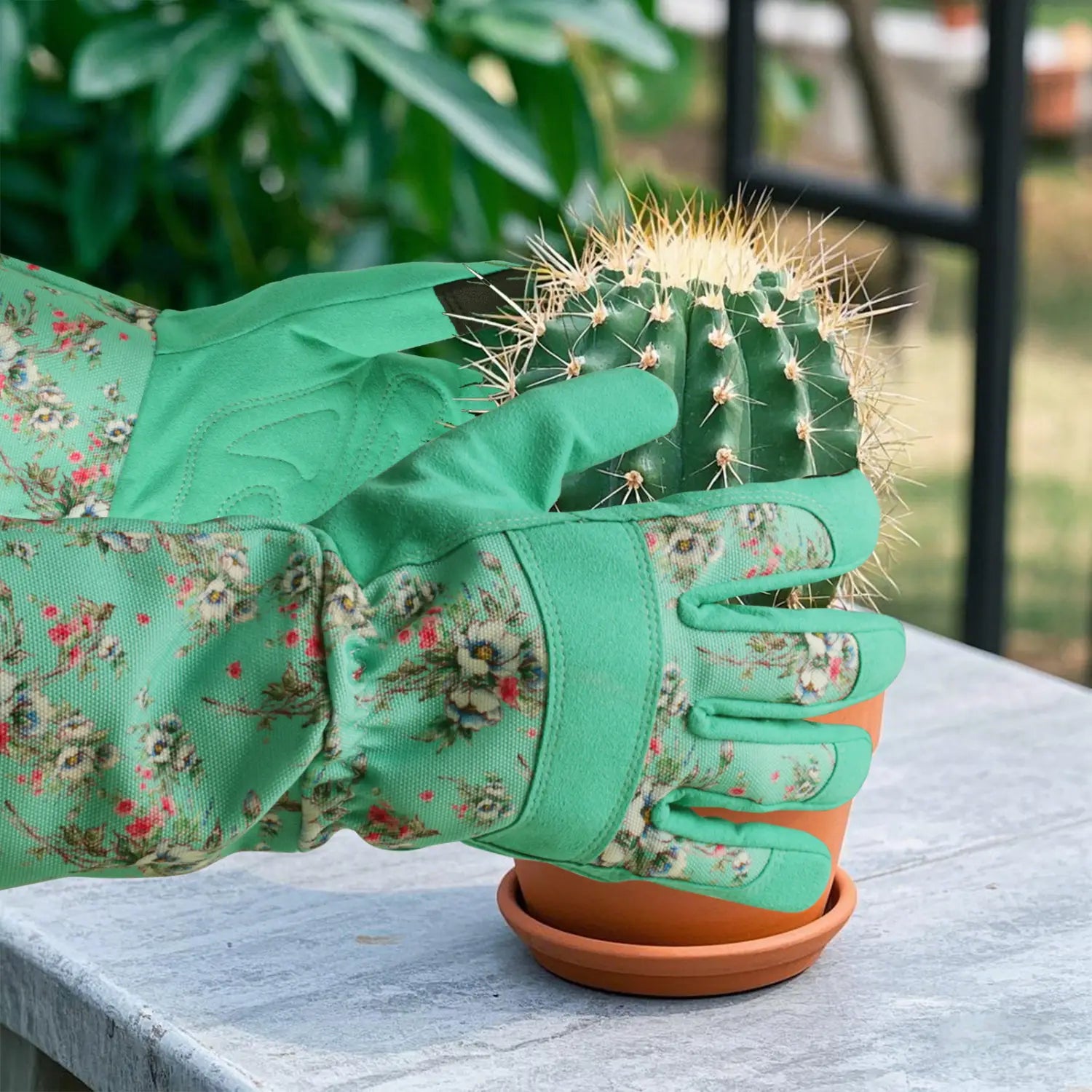 Gants de jardinage floraux verts pour femmes, respirants et anti-épines, qui bercent un cactus vert épineux dans un pot en terre cuite orange.