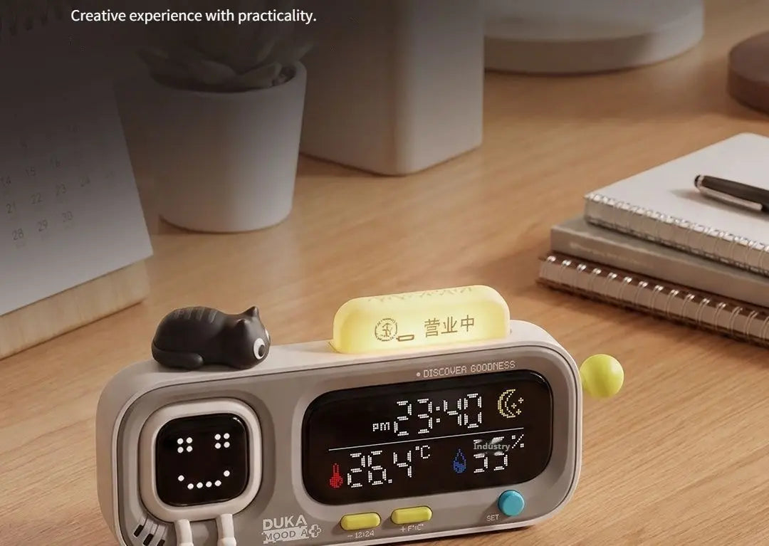 gray duka mooda smart digital alarm clock with smiling face display, smart temperature and humidity readings, and decorative cat figurine on top.