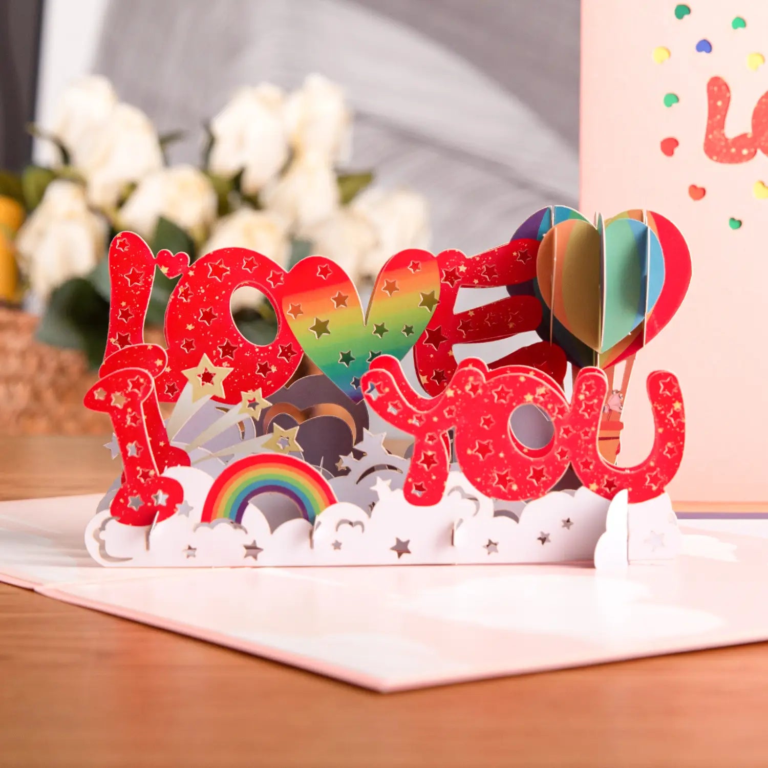 Carte de la Saint-Valentin 3D à effet pop-up vibrante rouge aux couleurs de l’arc-en-ciel, avec le texte « i love you », des détails d’étoile, une montgolfière et une base de nuages, pour des salutations romantiques en couple.