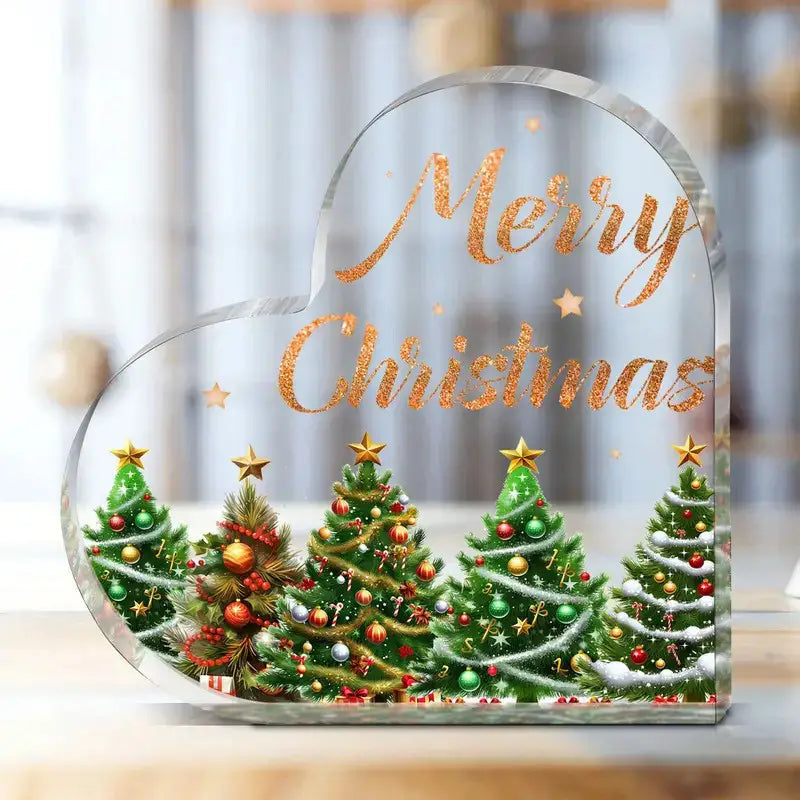 Soporte para adorno de escritorio en forma de corazón navideño de acrílico transparente, que presenta texto de “Feliz Navidad” en dorado brillante y cinco árboles verdes decorados con adornos rojos y dorados.