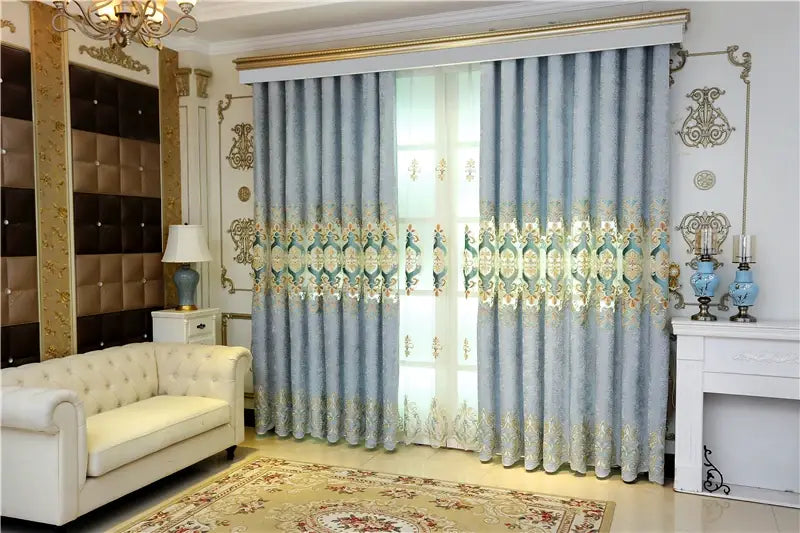 Light blue embroidered living room curtains with intricate gold and teal patterns hang elegantly across a French window.