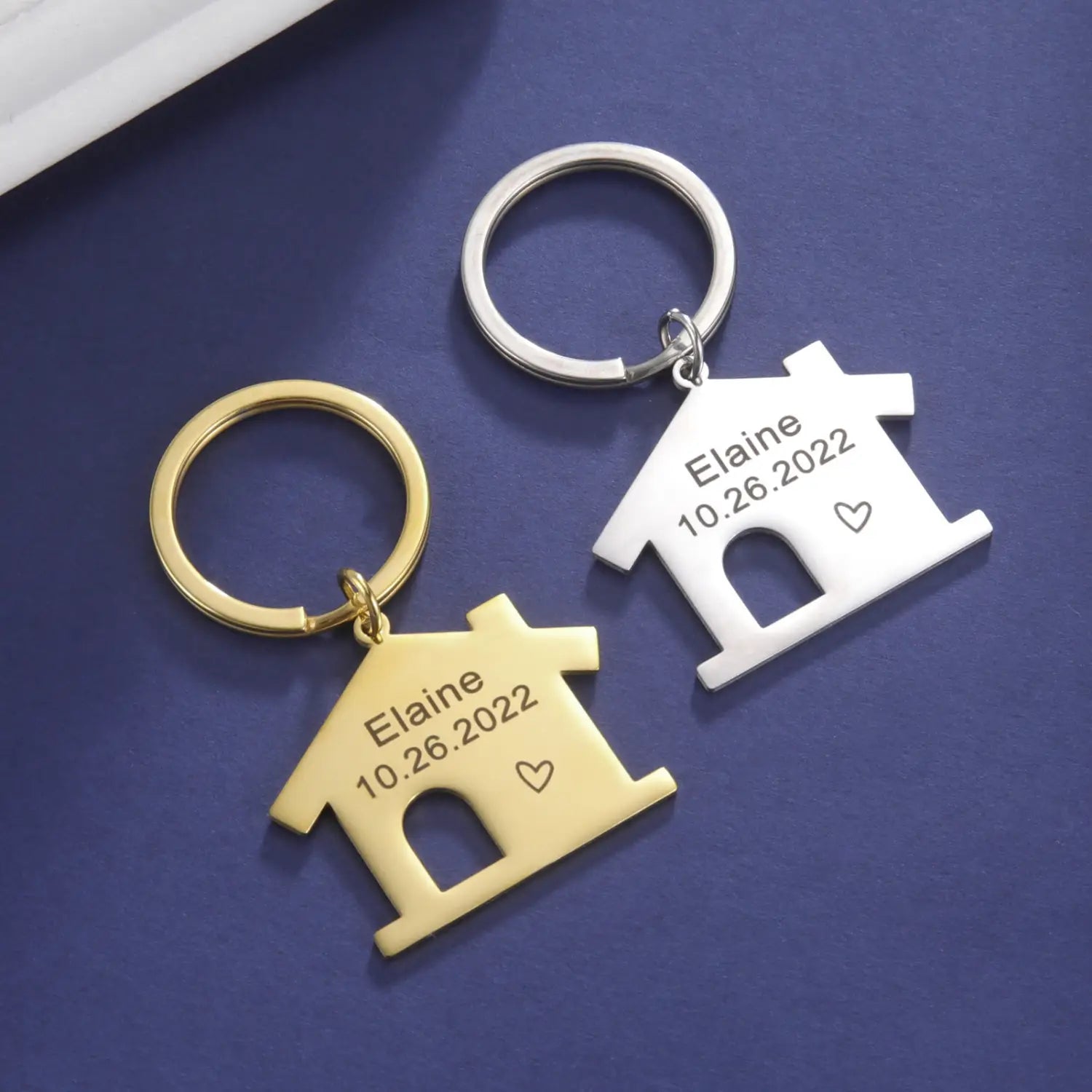Two personalized house keychain custom couple gifts in gold and silver metal each engraved with the name elaine the date 10.26.2022 and a small heart symbol.