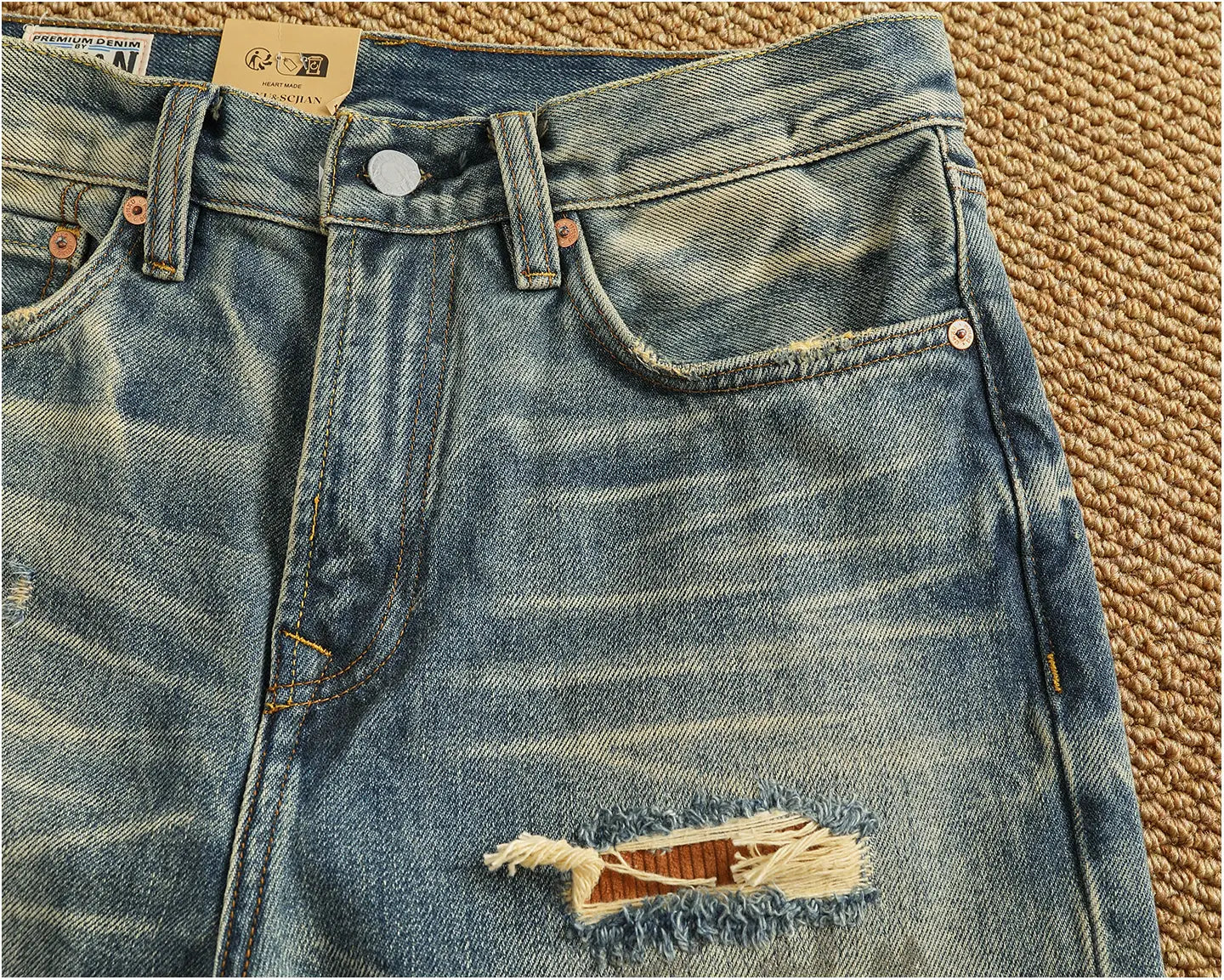 Distressed patchwork denim jeans men in blue with a faded wash and frayed tear at the thigh featuring copper-colored hardware.