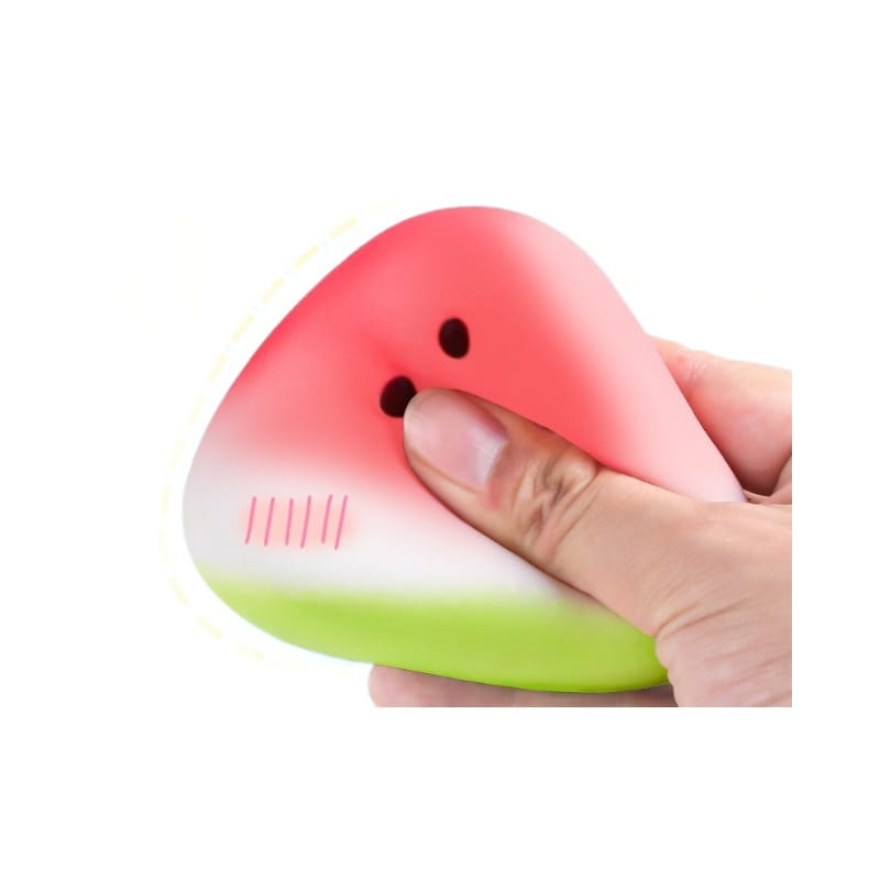 Une balle anti-stress souple et extensible en forme de pastèque, avec un extérieur dégradé rose et vert, des yeux à points noirs et des lignes évoquant des graines rouges sur sa partie blanche