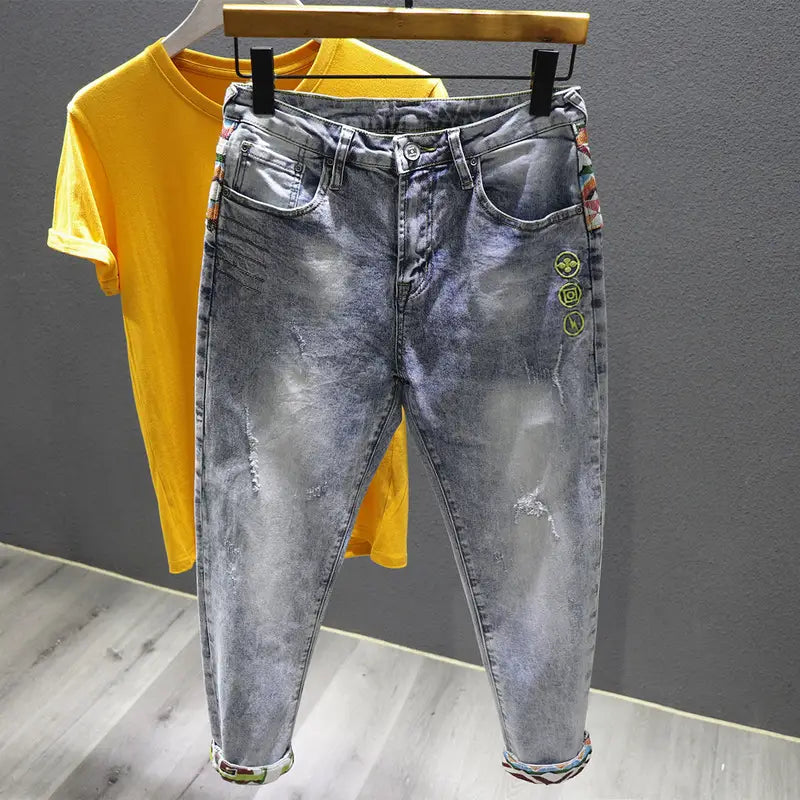 Men slim fit stretch white denim jeans in light wash with distressed details and colorful embroidered patches along the side seams and cuffs.