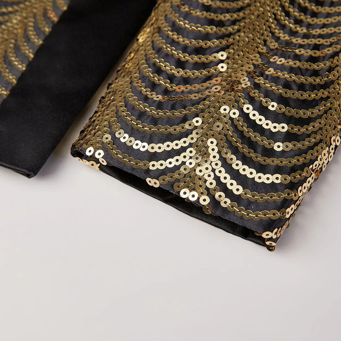 Black satin blazer for men featuring a sleeve adorned with intricate gold sequin concentric wave-like patterns.