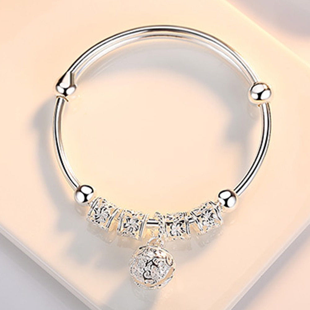 Bracelet jonc à billes grelots en argent sterling, avec un jonc en argent comportant des breloques au motif floral finement travaillé et un pendentif sphérique suspendu.