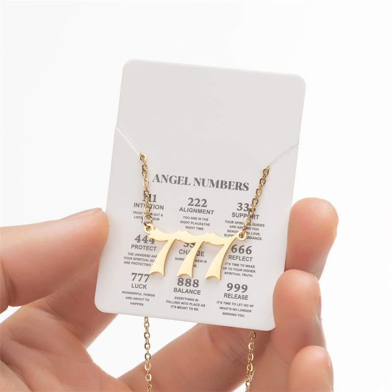Gold-toned necklace featuring a prominent 777 charm suspended from a delicate chain displayed on an angel numbers card.